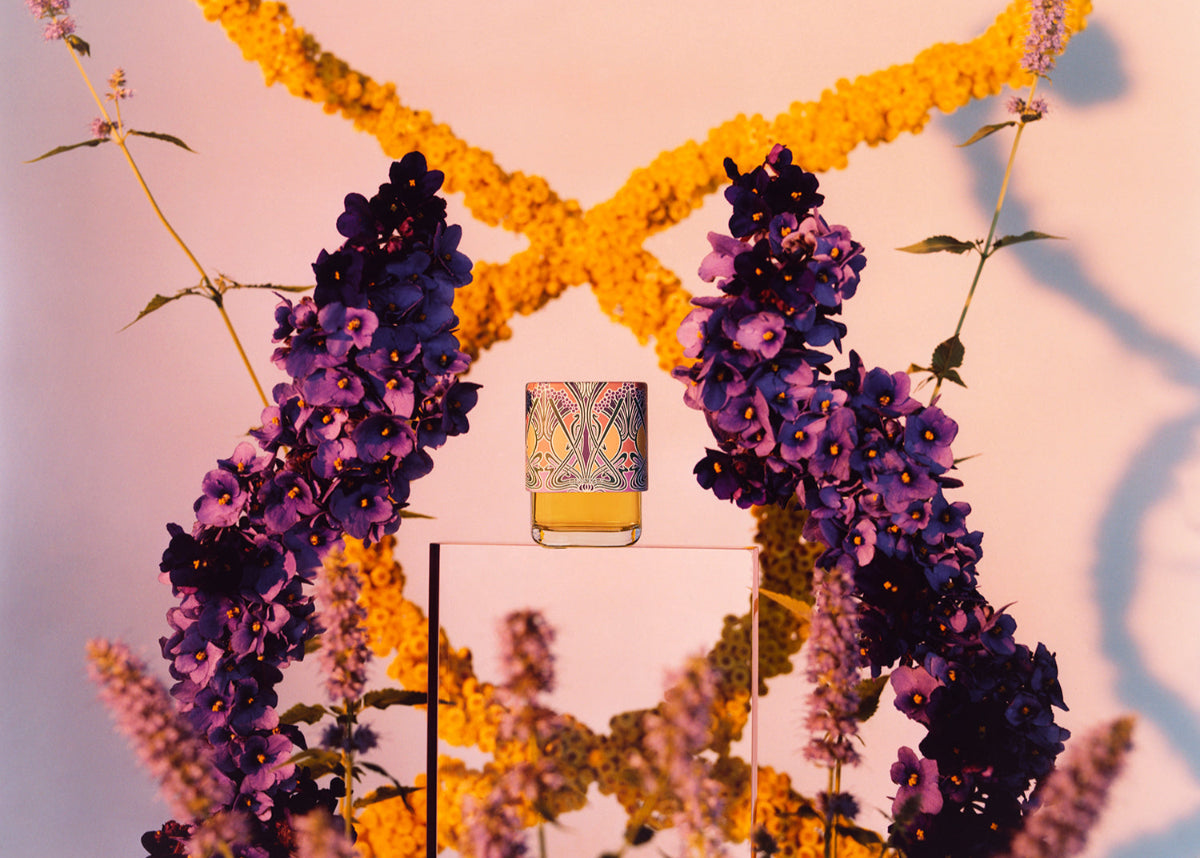 Decorative wreath with purple and yellow flowers and a Liberty Perfume Bottle in the center.