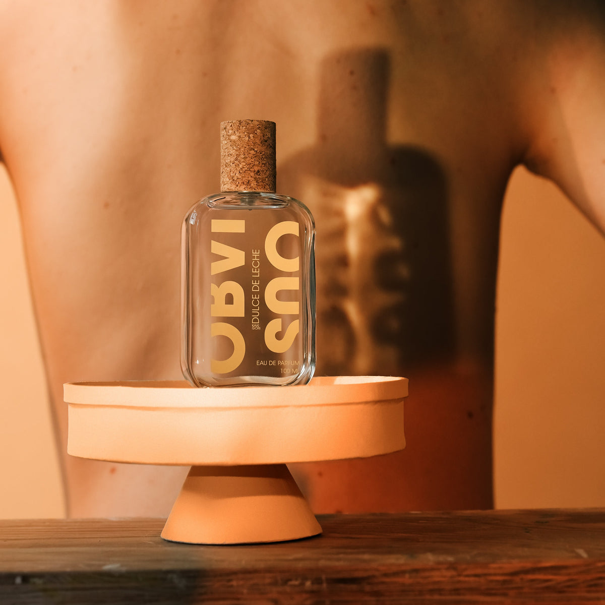 Perfume bottle on a wooden stand with a woman's back in the background