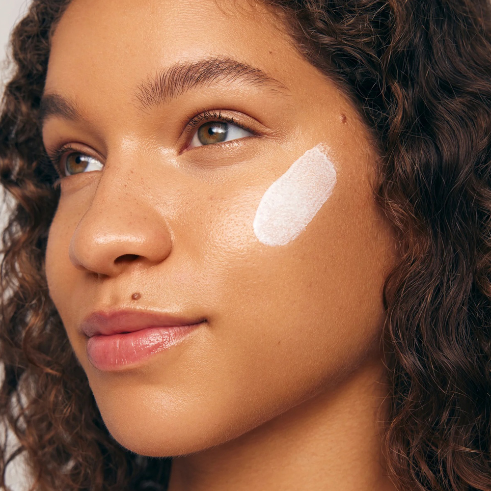 Close-up of a woman's face with a skincare product applied to her cheek.