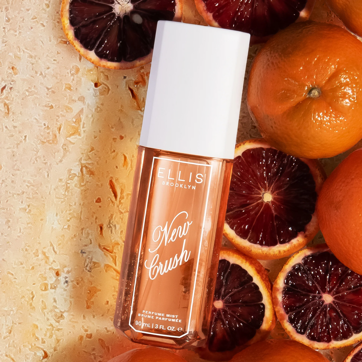 Ellis Brooklyn New Crush perfume bottle surrounded by sliced oranges on a textured surface