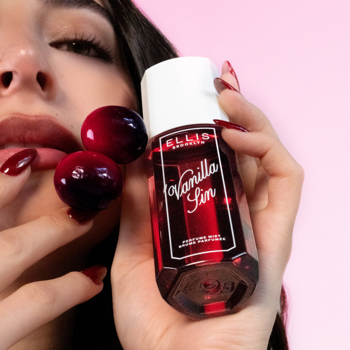 Hand holding a red Ellis Brooklyn Vanilla Sin perfume bottle with a pink background
