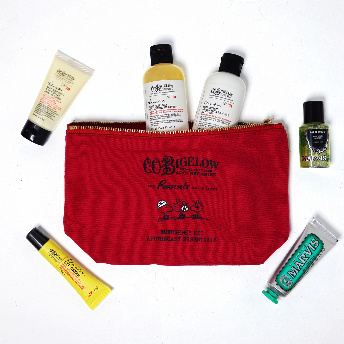 A red zippered cosmetic pouch with black printed branding sits on a white background, surrounded by assorted travel-sized toiletries including O'BGELOW bottles and tubes, a small green bottle, and a yellow tube.