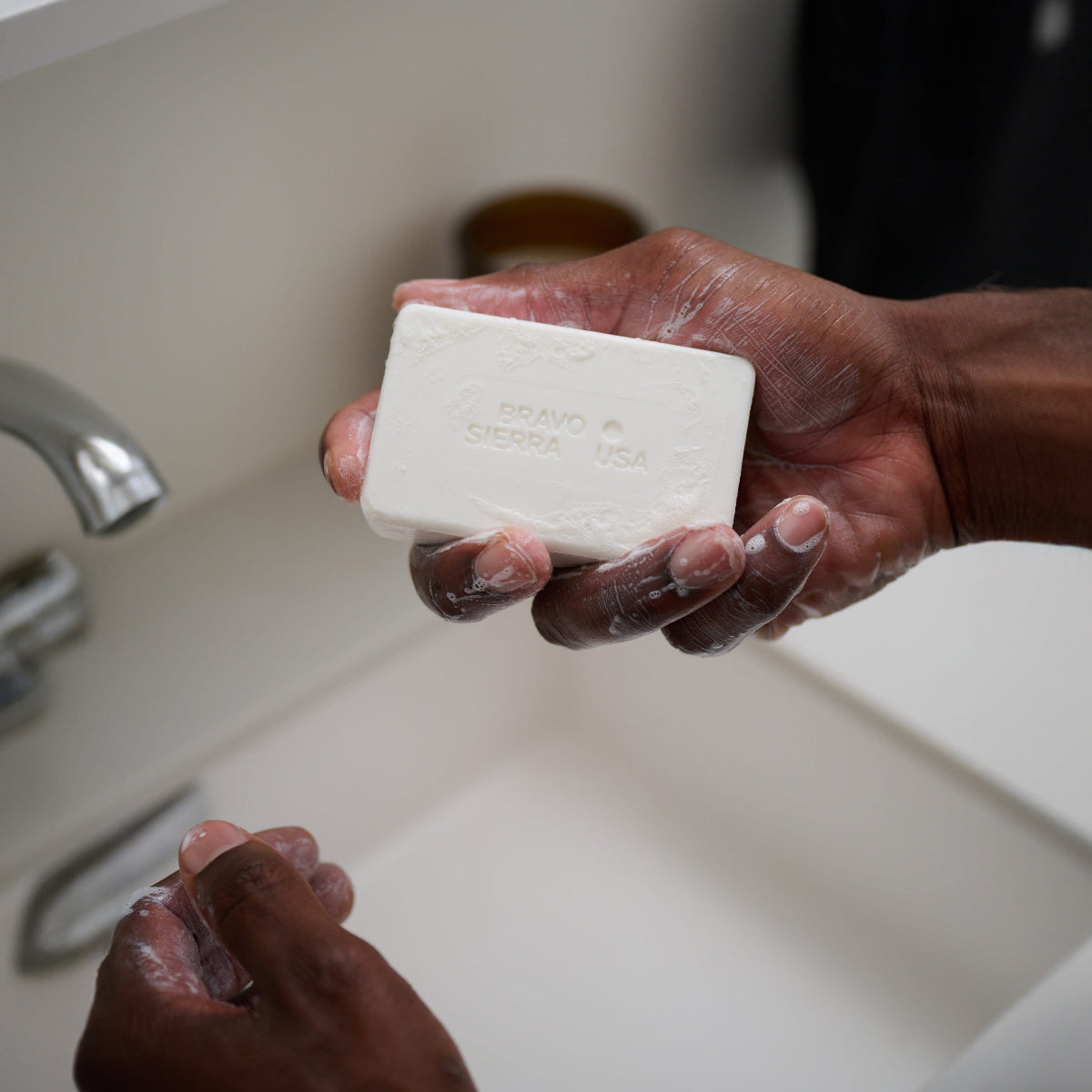 Soapy hands holding Bravo Sierra's Unscented Face & Body Cleansing Bar over a sink. 