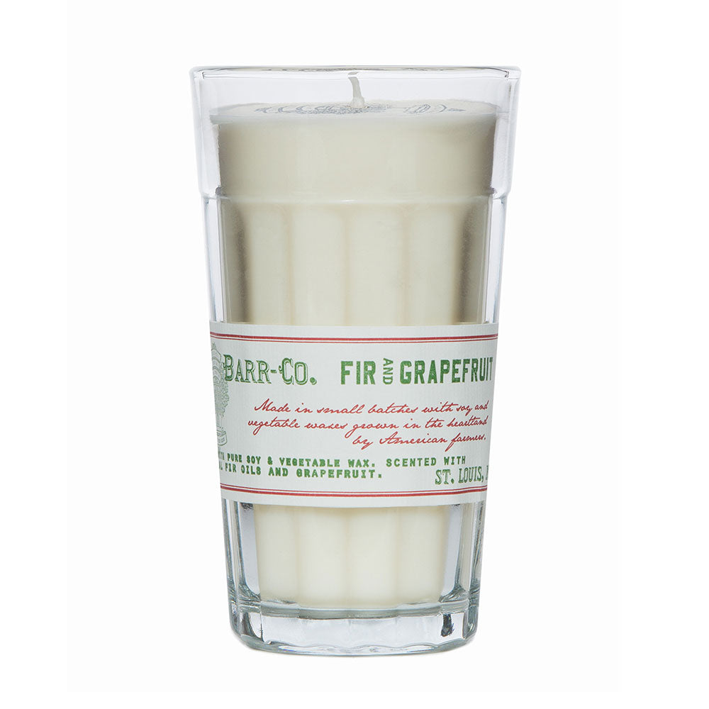 A clear glass candle with white wax, labeled 'Barr-Co. Fir & Grapefruit'.