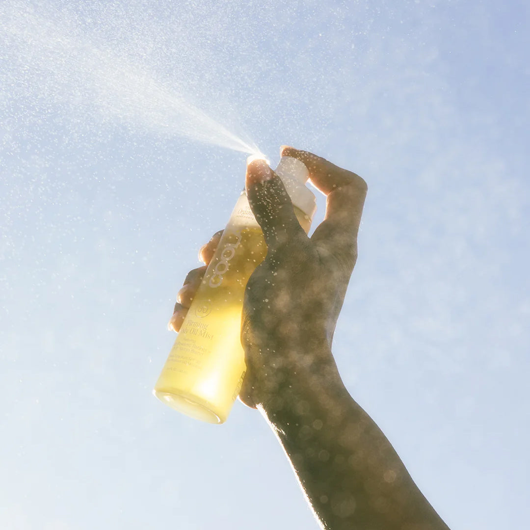 Hand spraying COOLA Firming Body Oil Mist product into the air