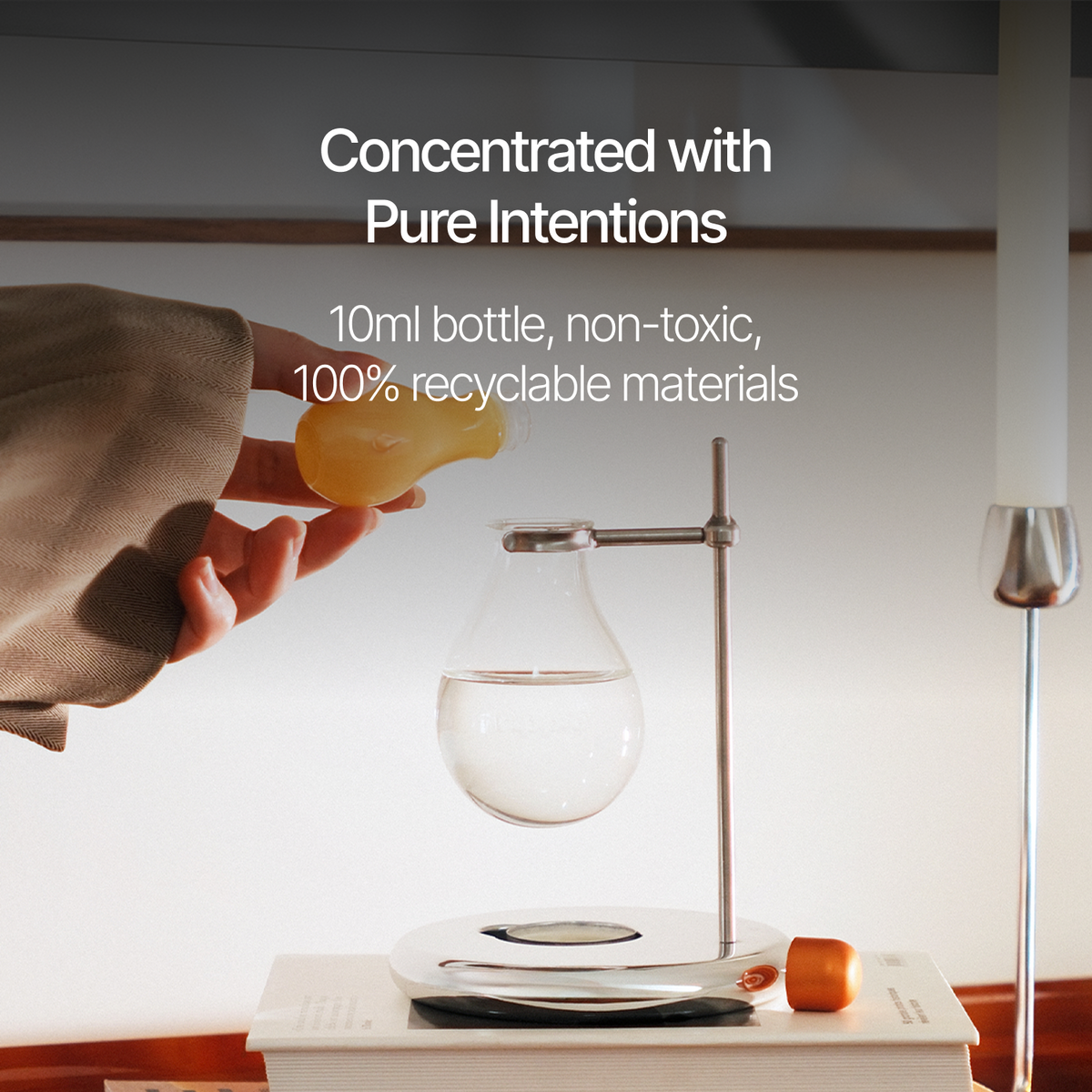 A hand pours liquid from a small yellow bottle into a clear floating teapot setup on a magnetic base, with overlaid text reading 'Concentrated with Pure Intentions' and '10ml bottle, non-toxic, 100% recyclable materials.'.