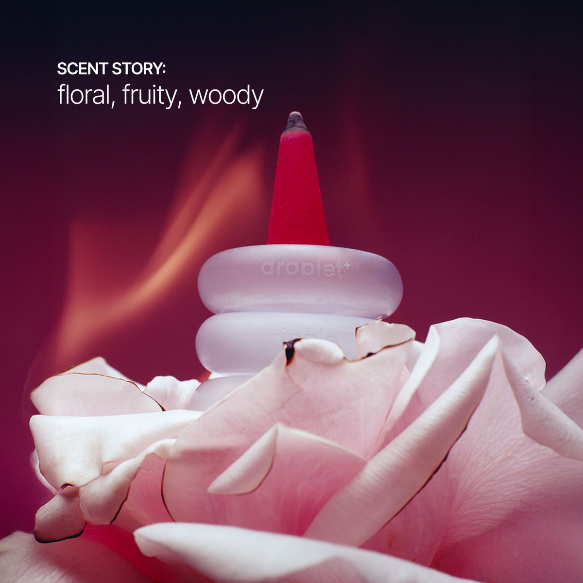 A close-up product photo of a droplet incense holder with a pink incense stick, set against a dark red and purple background with soft flame-like light effects and white text reading 'SCENT STORY: floral, fruity, woody'.