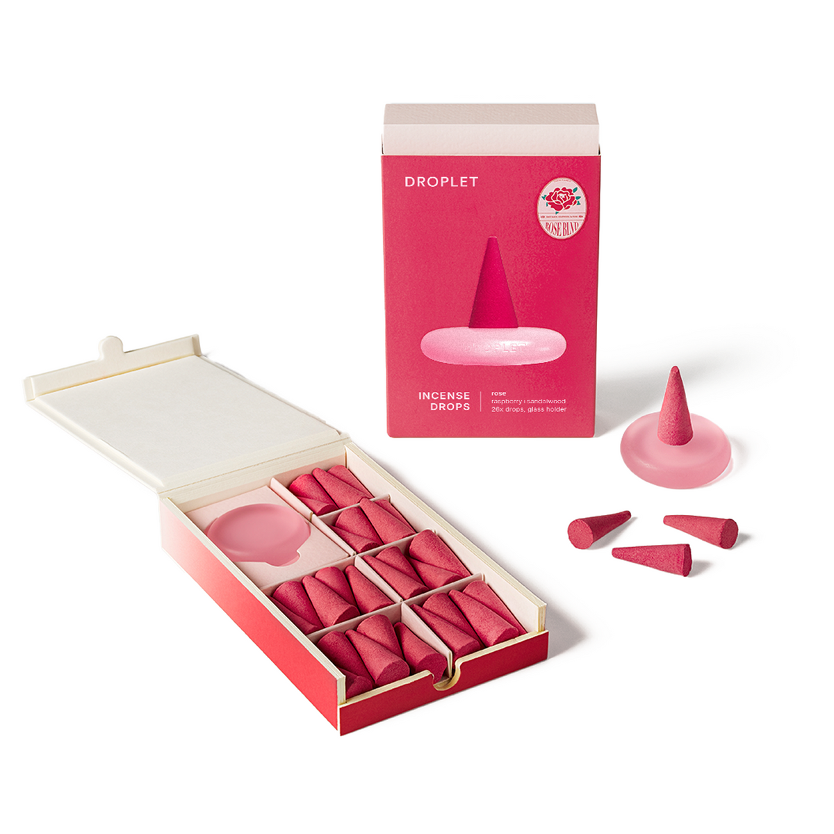 Pink incense drops set in an open red box next to its pink retail box and three loose incense cones on a white background.