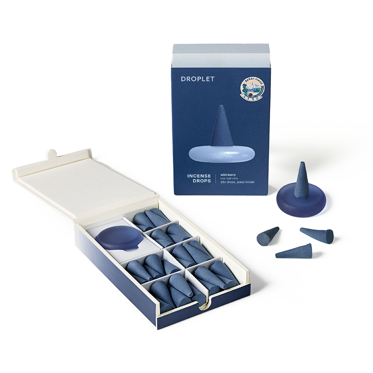 A boxed set of blue droplet-shaped incense drops shown open with several drops arranged beside it, alongside the retail box. The packaging is dark blue and cream, and the incense pieces are a muted medium blue.