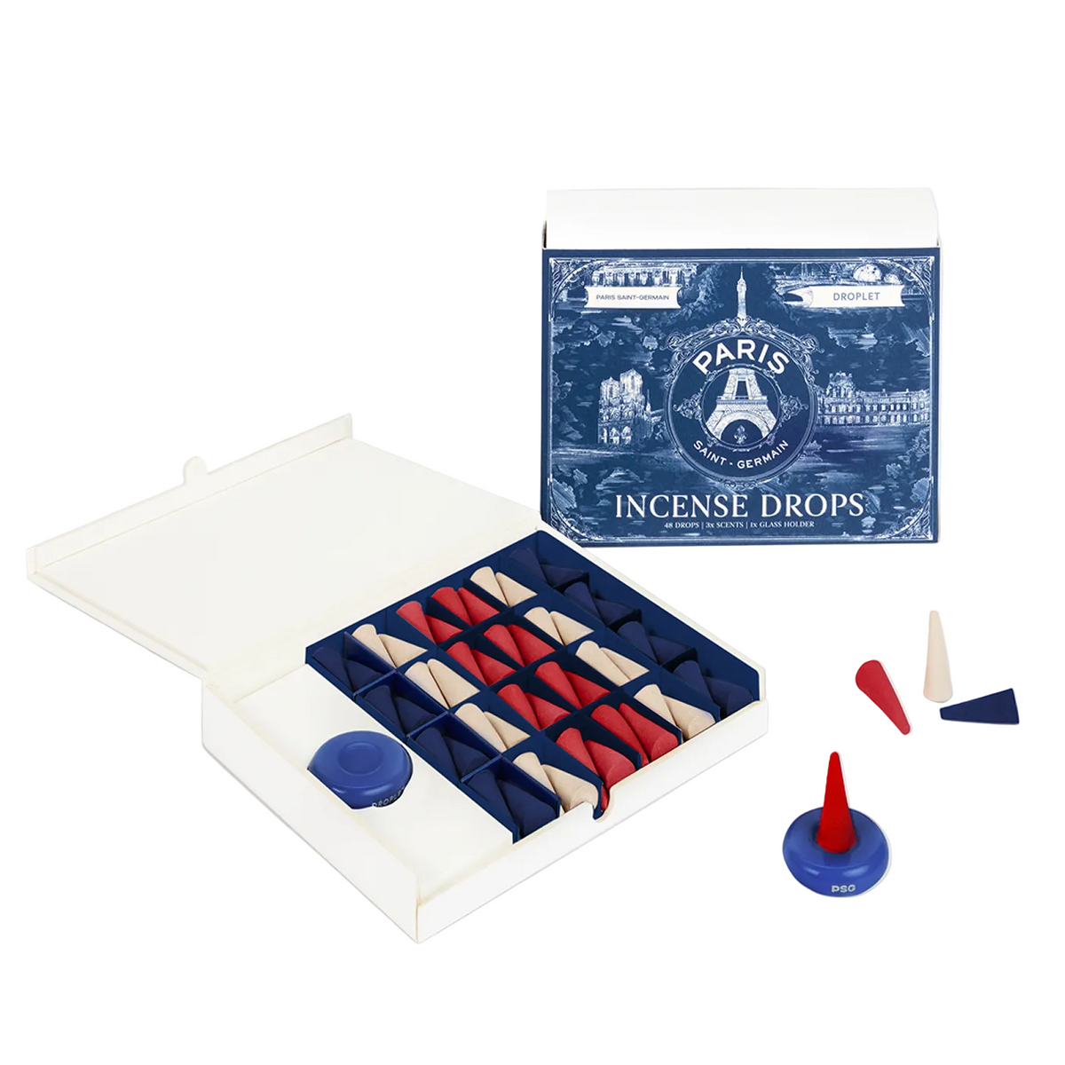 A boxed set of Paris-themed incense drops shown open, with the retail box standing behind it on a light gray background. The set includes multiple small cone-shaped incense sticks arranged in a dark tray, a blue circular piece, and a few loose incense pieces outside the box.