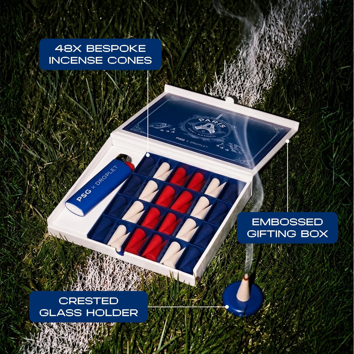 An open white and navy presentation box containing 48 bespoke incense cones, shown on grass with smoke rising. The box is labeled '48X BESPOKE INCENSE CONES' and includes a blue incense stick, an embossed gift box, and a crested glass holder.
