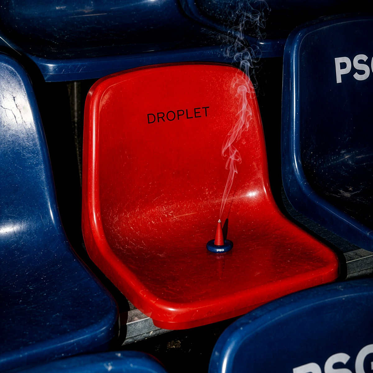 A red plastic stadium-style seat in the middle of a row of blue seats, with the word 'DROPLET' printed on it and a small smoking object resting on the seat.