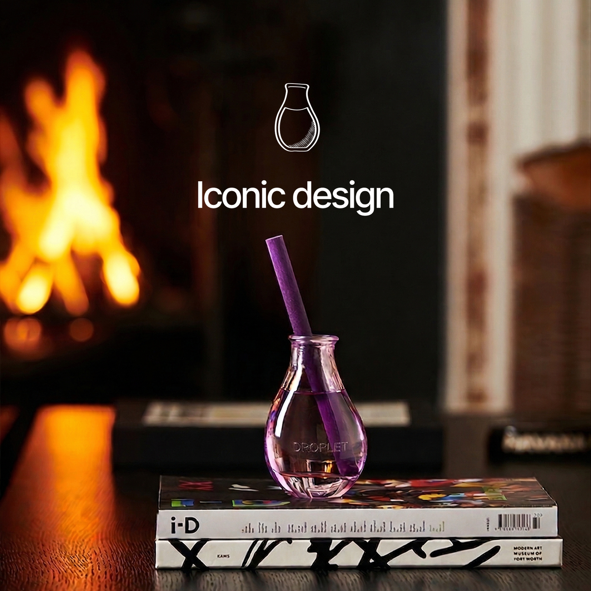 A small clear glass vase with a purple straw sits on top of two books in a warm indoor setting with a blurred fireplace in the background. White text above reads 'Iconic design' with a simple outline of the vase.