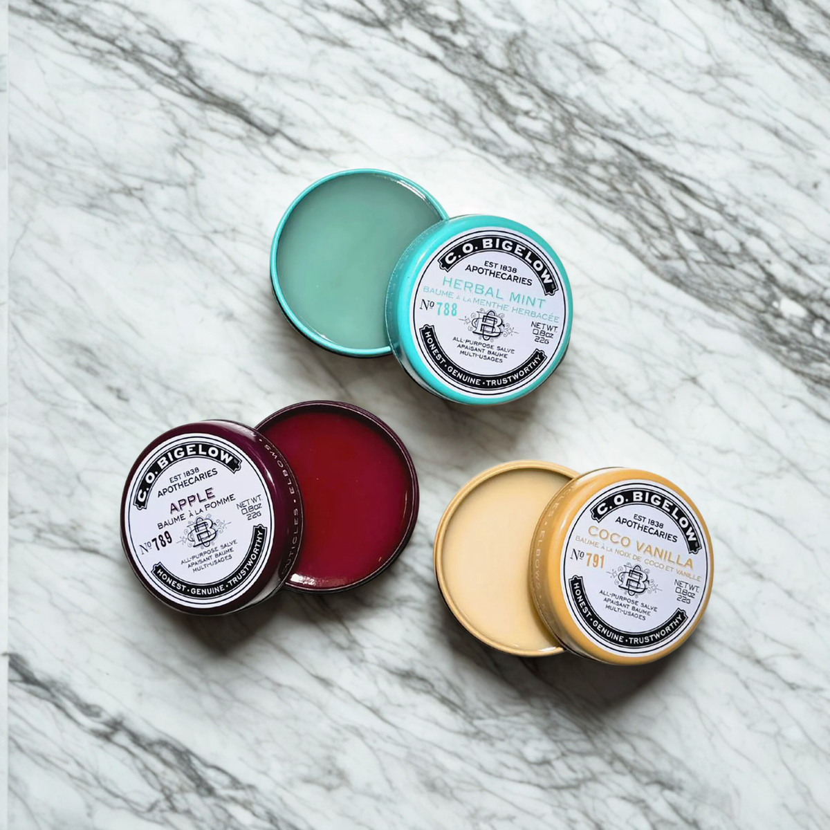 Five small containers of C.O. Bigelow Salve Tins on a marble surface