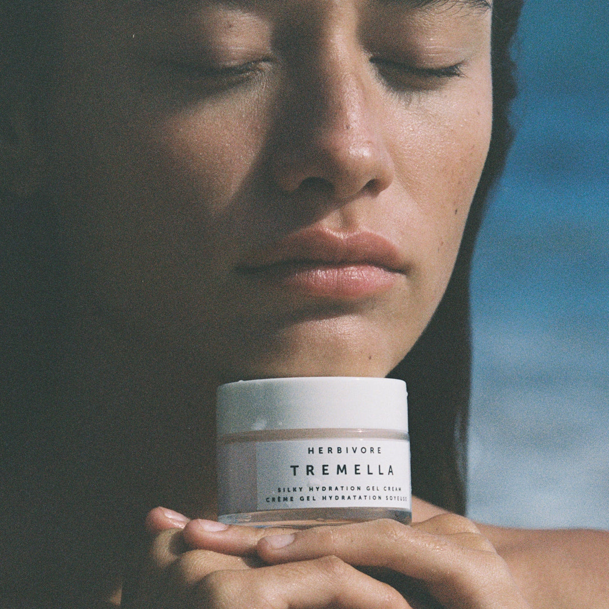 Person holding a jar of Herbivore Tremella product against a blurred natural background