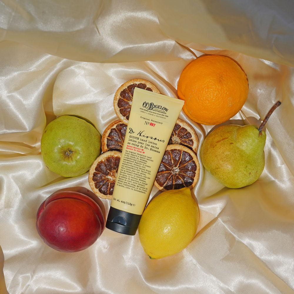 Co Bigelow Dr Hiousous Hand Lotion No 007 along yellow silk background surrounded by lemon, pear, orange, apple 