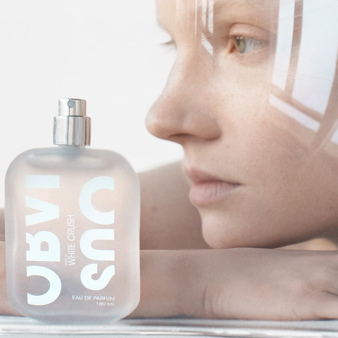Woman's face with a bottle of White Crush perfume in the foreground