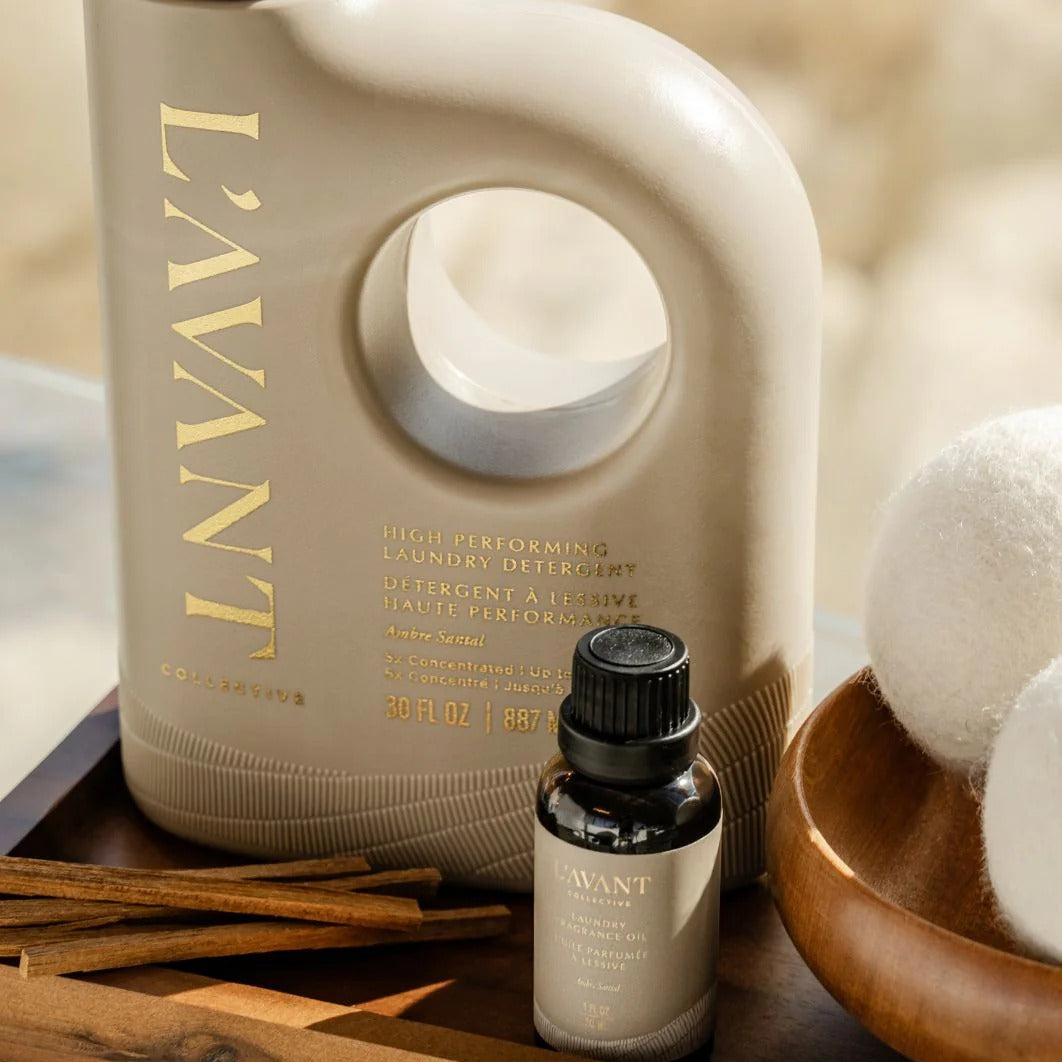 L'AVANT laundry detergent bottle and essential oil bottle on a wooden surface with white balls and cinnamon sticks.