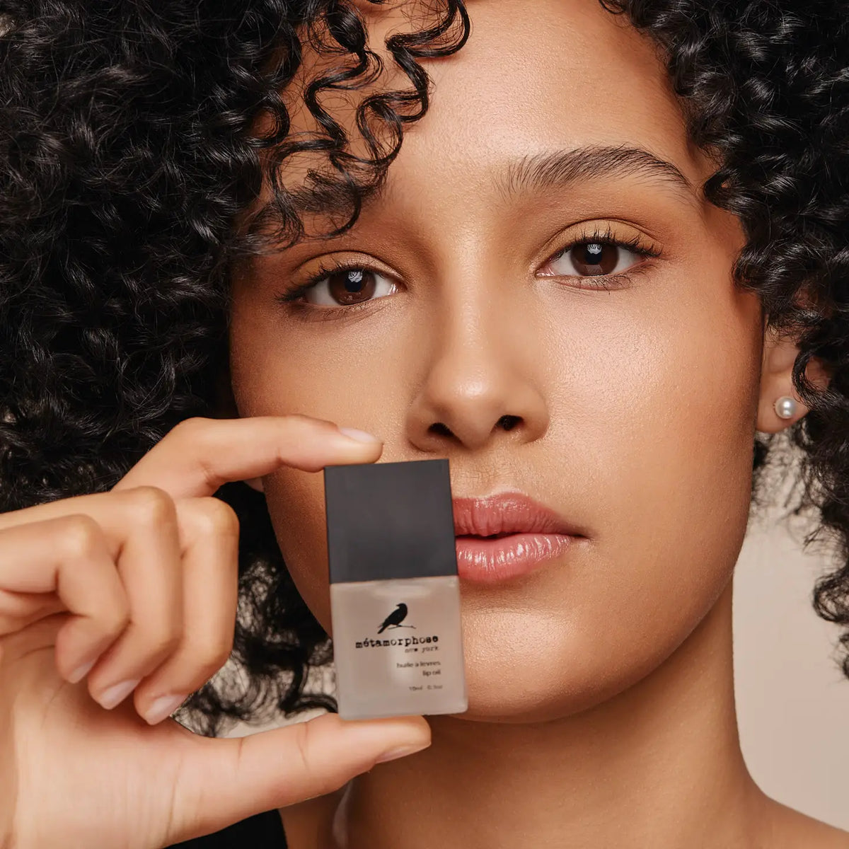 Woman holding Metamorphose Lip Oil in front of her face. 