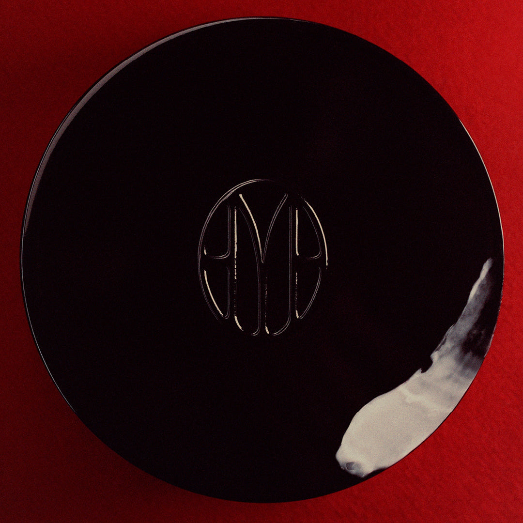 Overhead shot of Mienne Body Creme jar covered with a swipe of the body cream on top of a red surface. 
