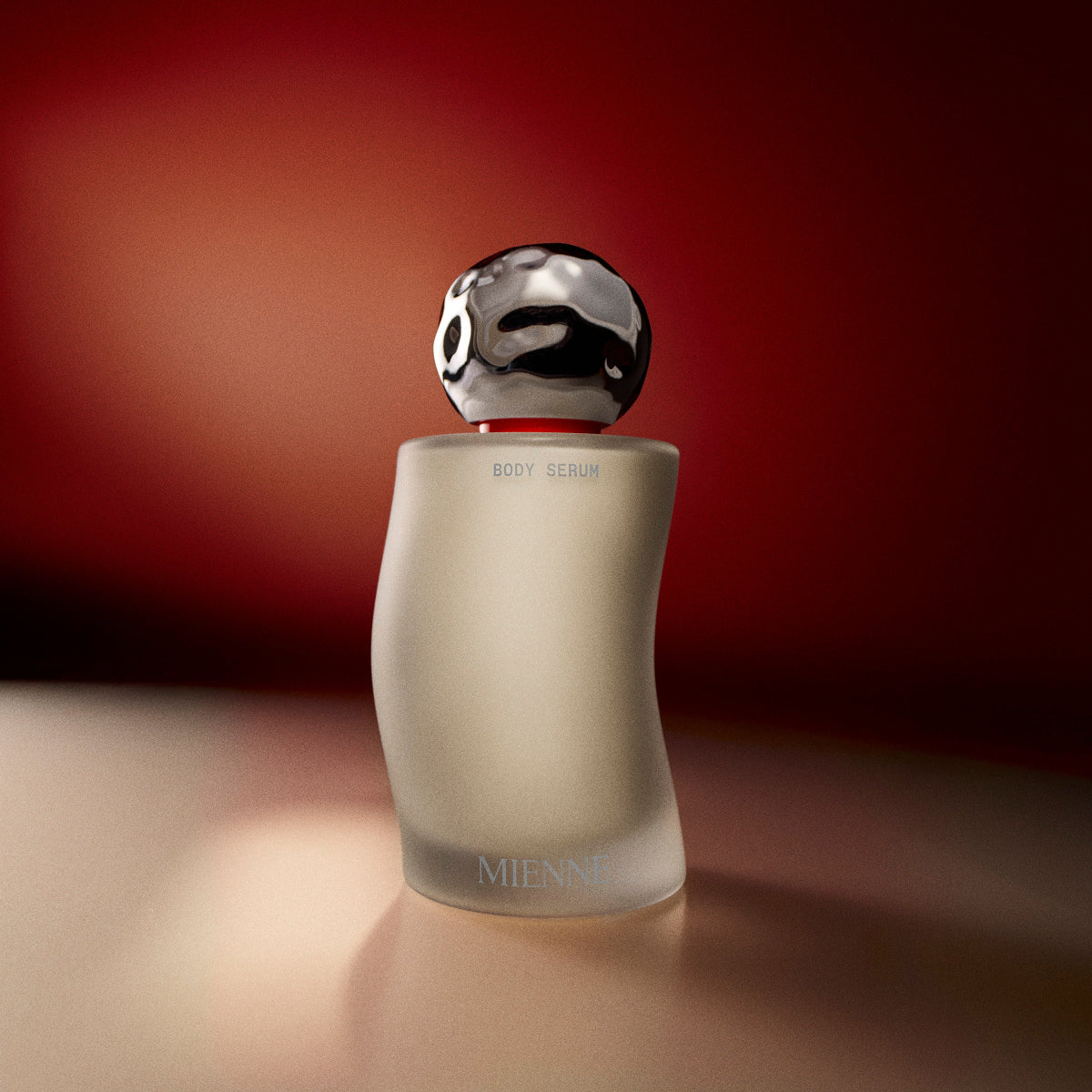 Mienne Body Serum bottle on a tan surface in front of an illuminated red background.