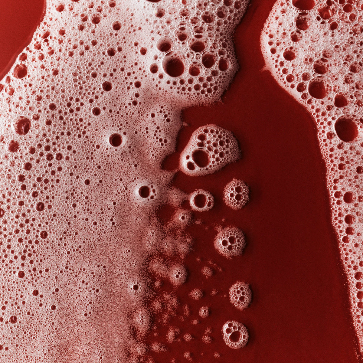 Closeup of soap suds from Mienne Body Wash on a red surface