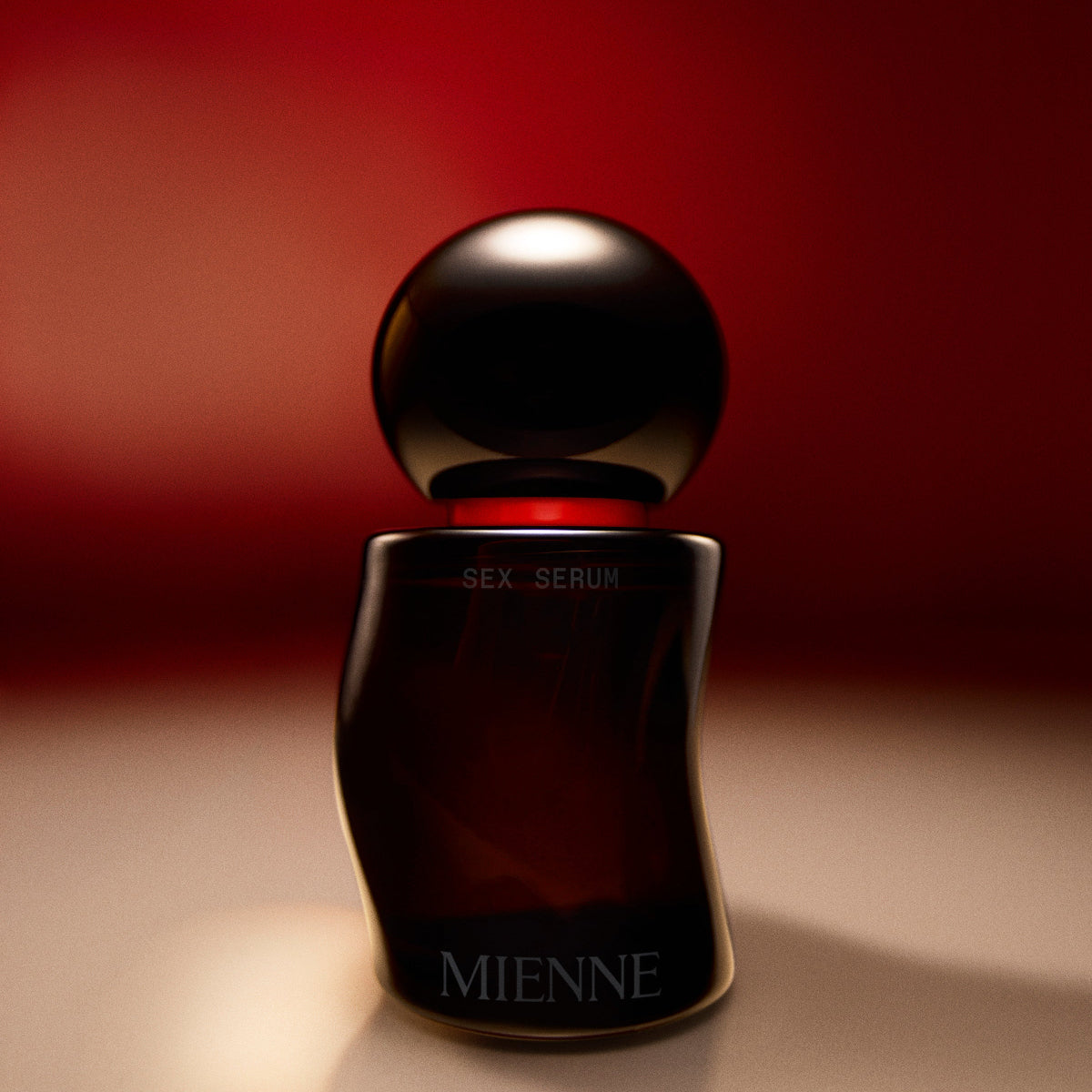 Mienne Sex Serum bottle on a tan surface in front of a red background.