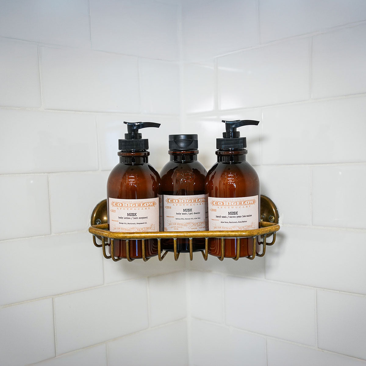 C.O. Bigelow Musk Body Lotion, Body Wash, and Hand Wash on a brass shelf in a bathroom shower. 