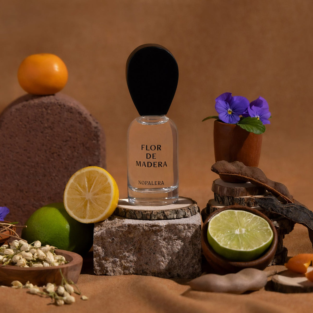 Perfume bottle labeled 'Flor de Madera' surrounded by fruits and flowers on a brown background