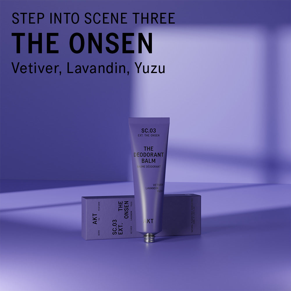 AKT The Onsen scented Deodorant Balm standing on and in front of a purple surface. Text overlaid on the image above the product reads "Step into scene three. The Onsen. Vetiver, Lavandin, Yuzu."