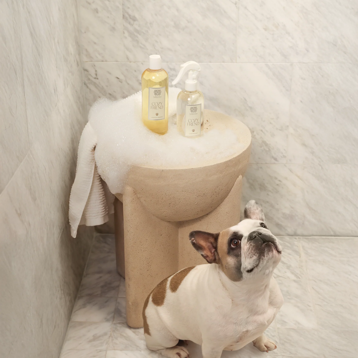 Dog standing next to a small round sink with bottles on top in a bathroom setting.