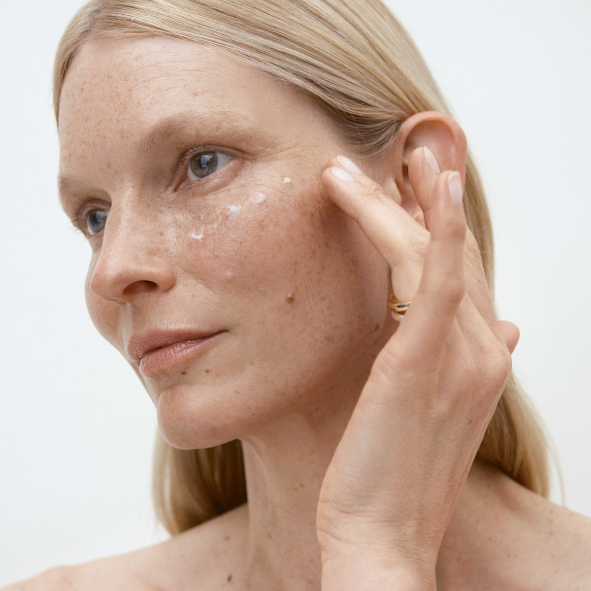 Woman applying cream to her face with a neutral background