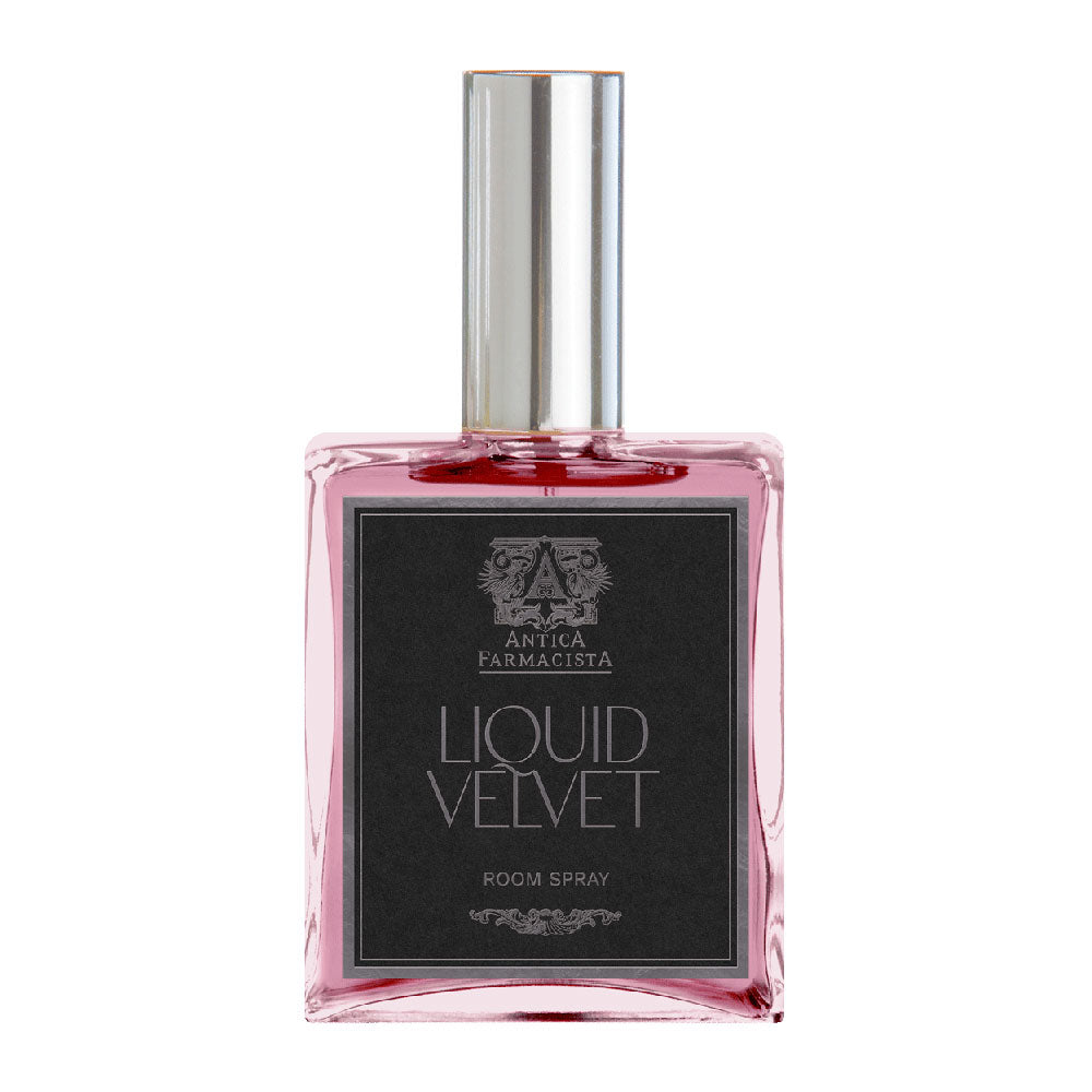 A clear glass bottle with a pink liquid inside, labeled 'Liquid Velvet Room Spray' with a silver cap and black label.