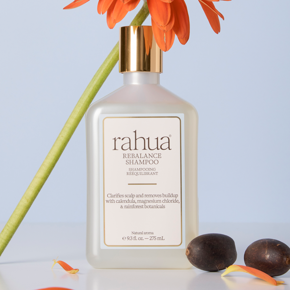 Rebalance Shampoo bottle with natural and floral items around it on a neutral background