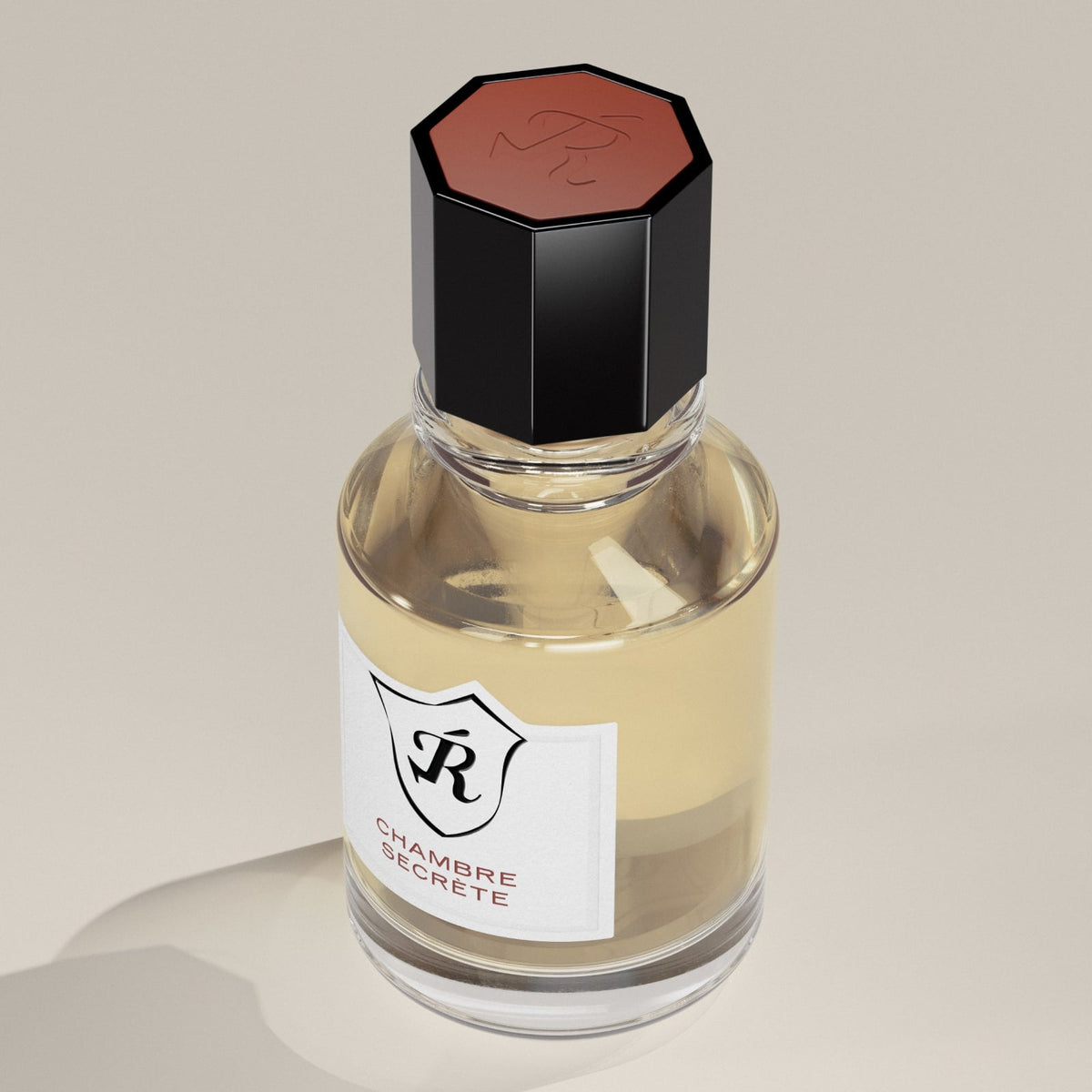 Perfume bottle with a black cap and 'Chambre Secrète' label on a beige background
