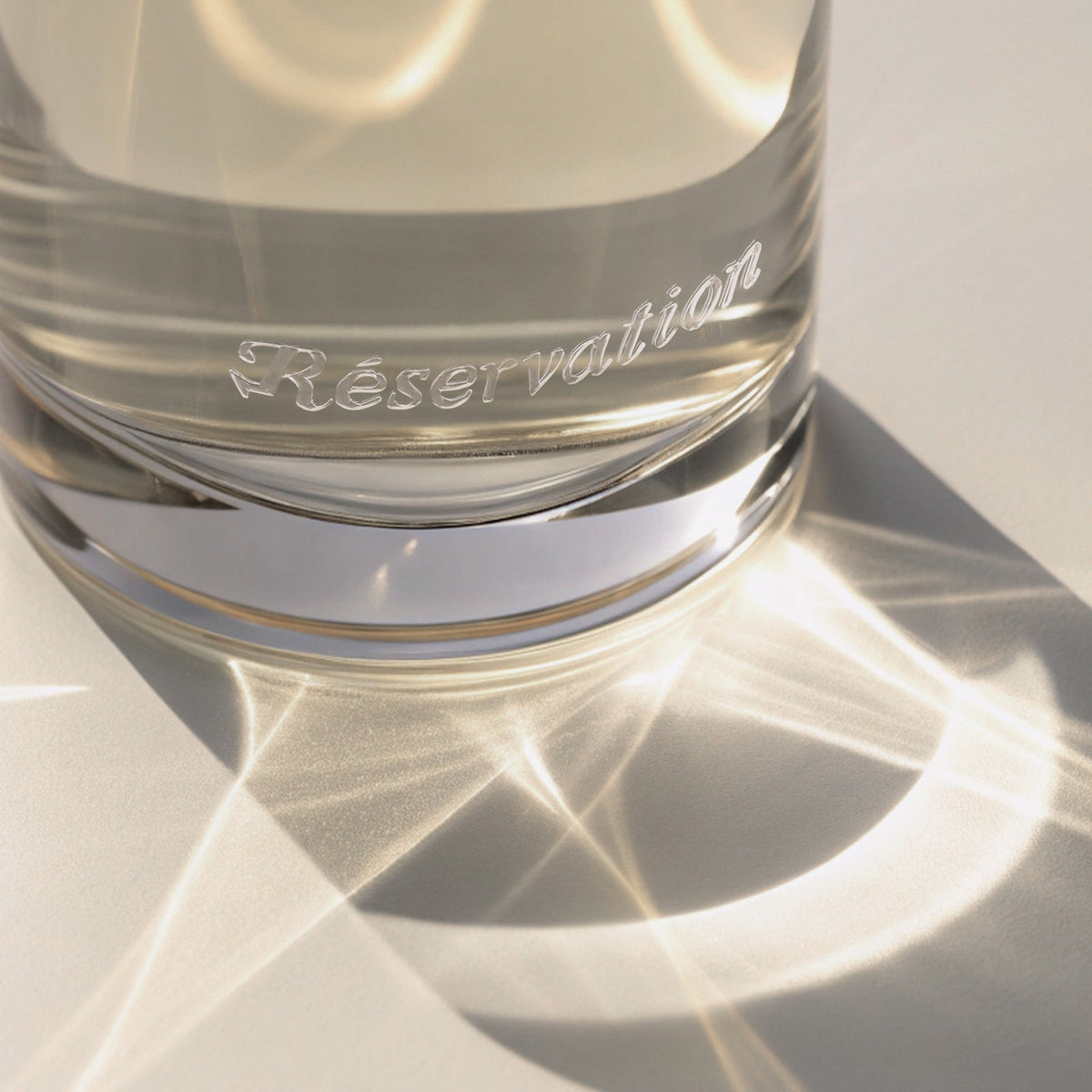 Light reflecting off a glass perfume bottle with 'Réservation' branding.