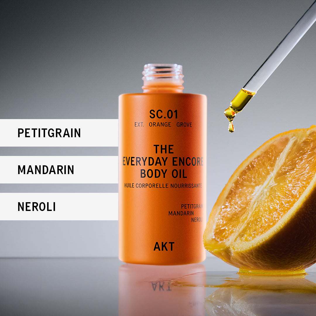 Orange body oil bottle with dropper and orange half on a reflective surface