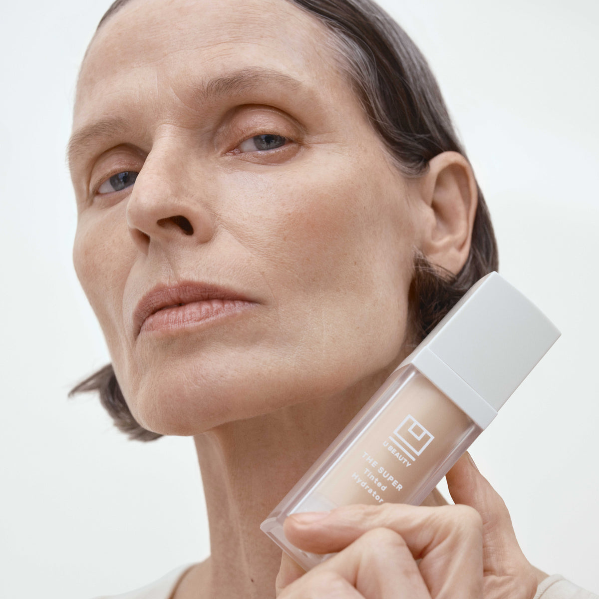 Woman holding a skincare bottle with a neutral background