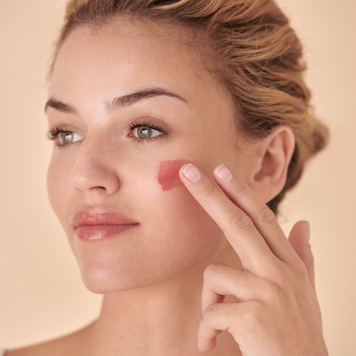 Woman applying Embryolisse Radiant Complexion Cream in Rose Glow.