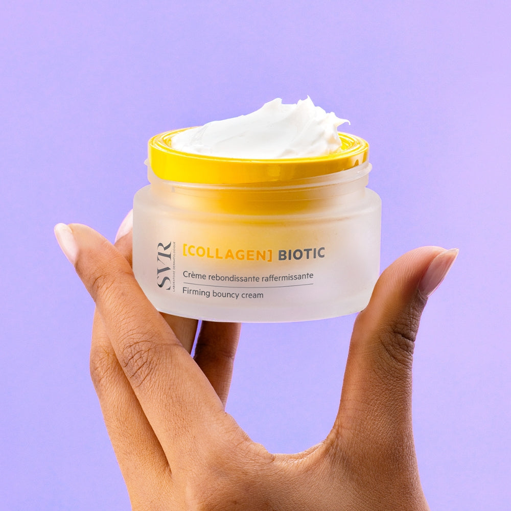 Hand holding a jar of SVR Collagen Biotic cream against a purple background