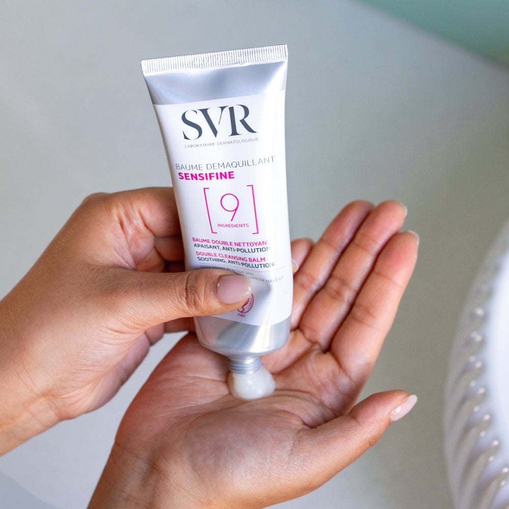 Hand holding a tube of SVR Sensifine Cleansing Balm product against a neutral background