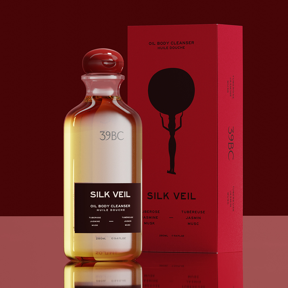 A Bottle of 39BC Silk Veil Oil Body Cleanser with amber liquid and a black label, standing in front of a red product box on a dark red reflective surface.