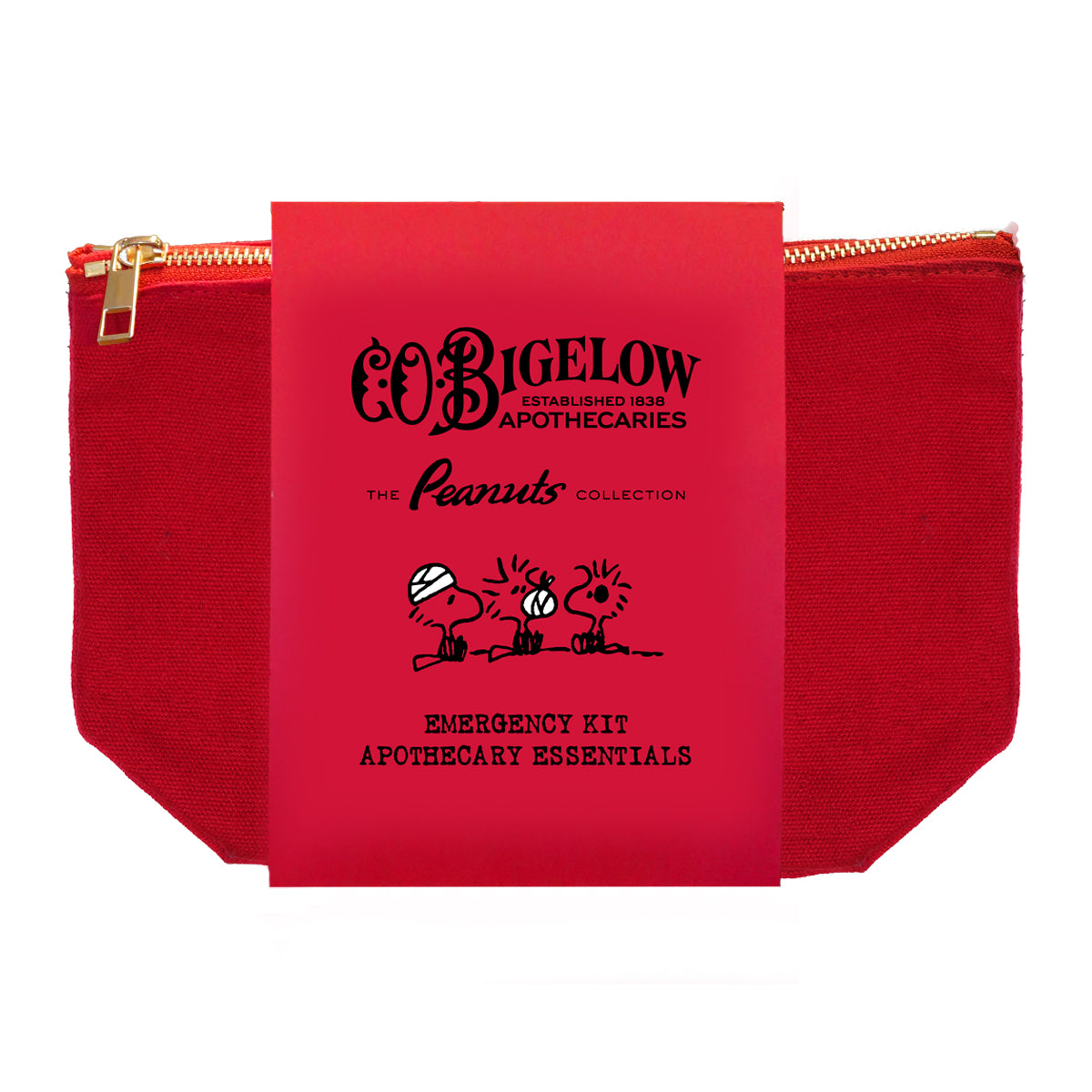 A red fabric zippered pouch with a gold zipper, held together by a bright red paper band labeled 'COBIGELOW The Peanuts Collection Emergency Kit Apothecary Essentials' with black cartoon illustrations.