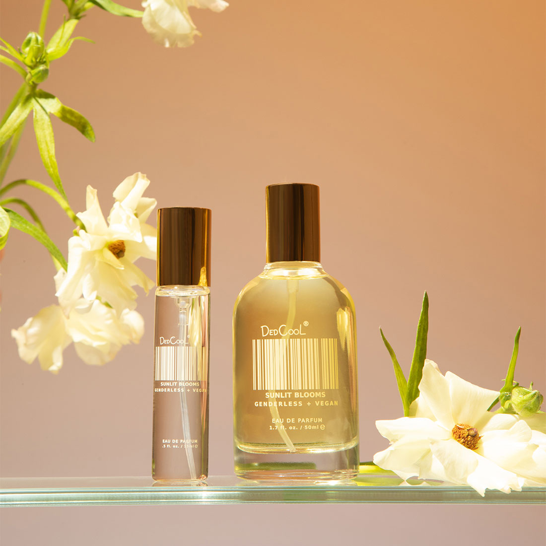 Sunlit Blooms EDP Travel and full size on a glass shelf with flowers.