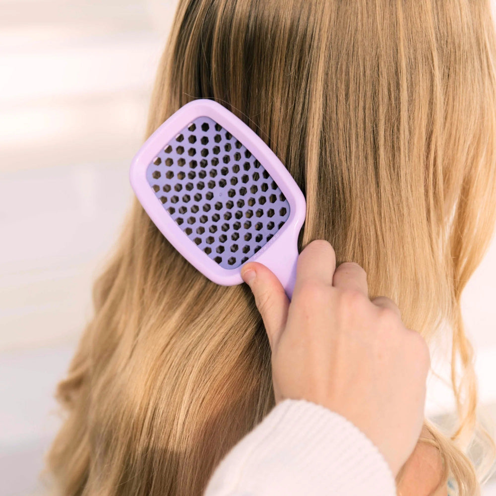 Person using a purple brush on their long blonde hair.
