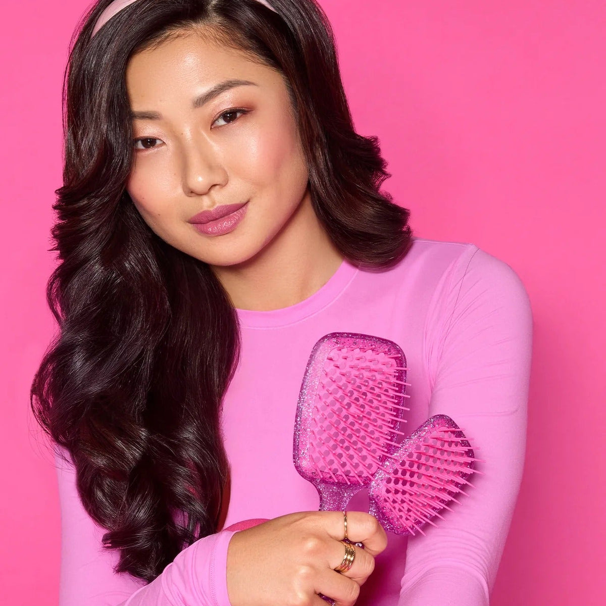 Woman holding a pink hairbrush against a pink background