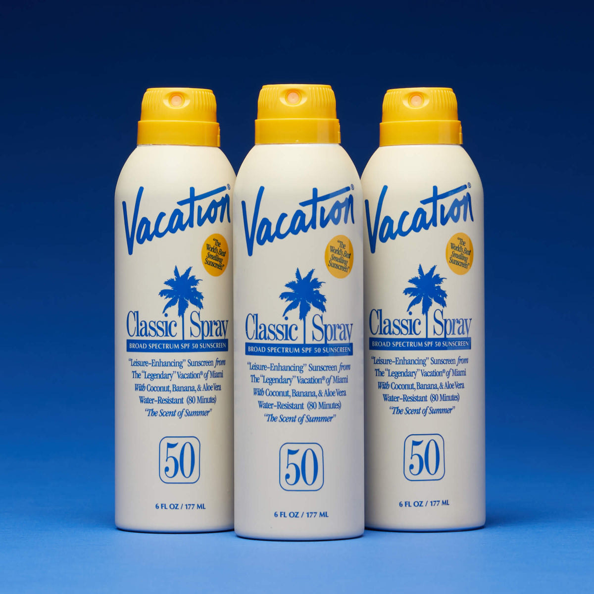 Three bottles of Vacation Classic Spray sunscreen on a blue background