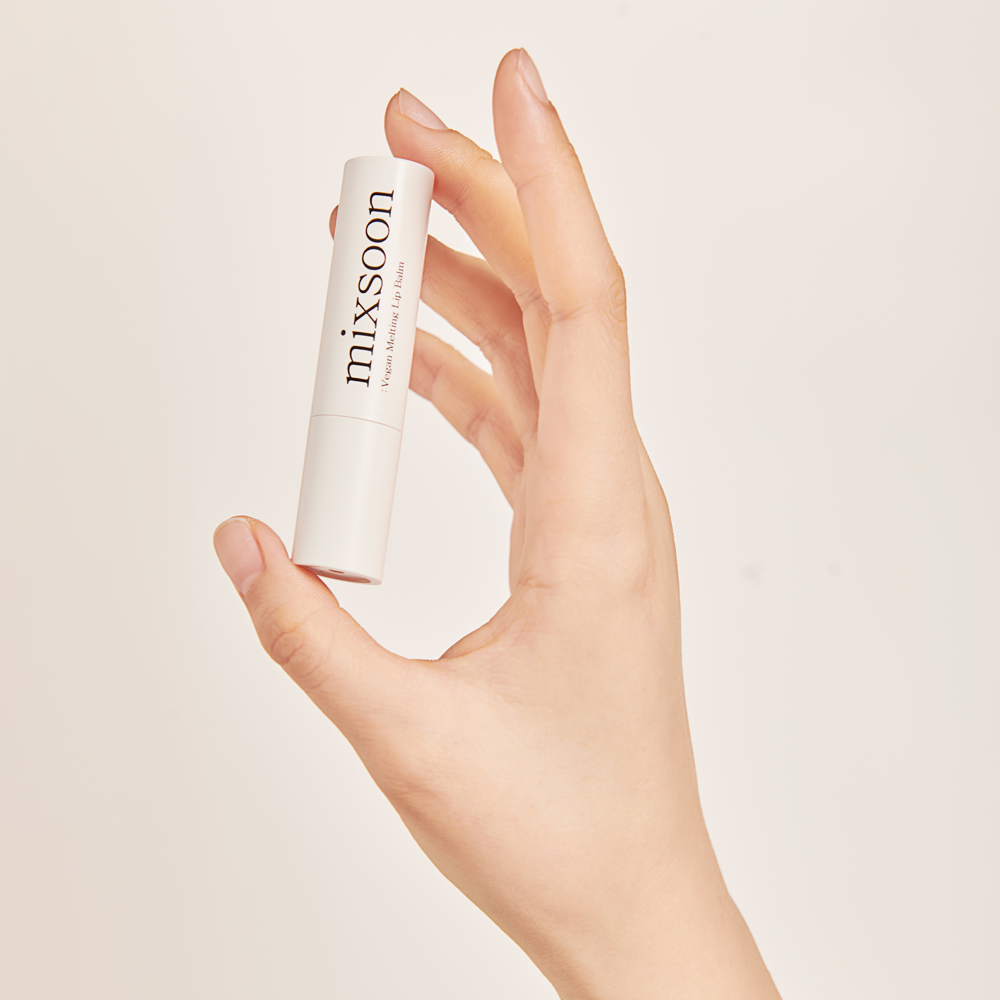 A hand holding mixsoon Vegan Melting Lip Balm - Dry Rose set against a solid off-white background.