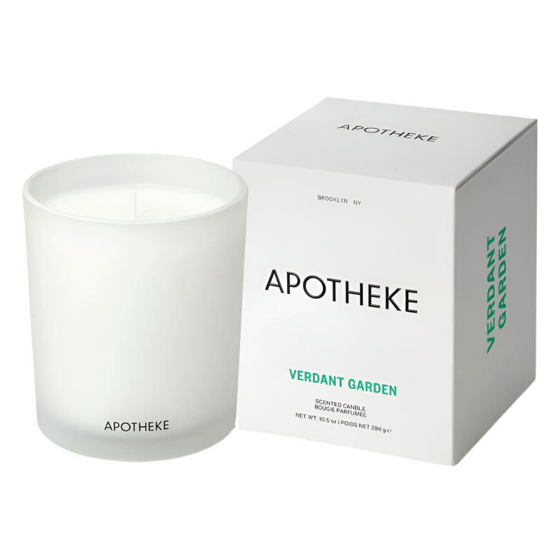 A white candle with green text on the box that reads 'APOTHEKE VERDANT GARDEN'. The candle is unlit, with a matte white finish and sits in front of its packaging.
