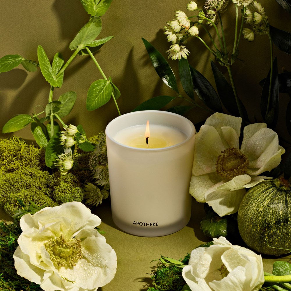 A white candle amongst flowers and plants.
